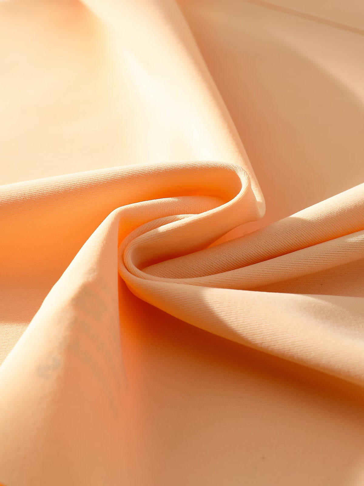 A close-up of peach-colored fabric draped in soft folds, showing its smooth texture and warm tone under directional light.