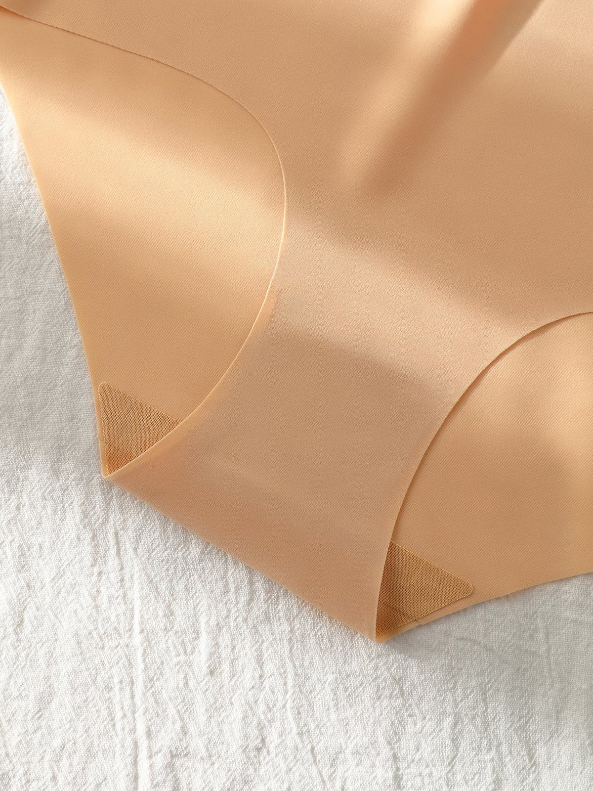 Close-up of a peach-beige sheer mesh fabric, likely a panty or underwear leg, laid flat on a textured white fabric background.