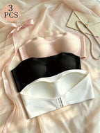 Set of three bras in pink, black, and white on a soft fabric background.