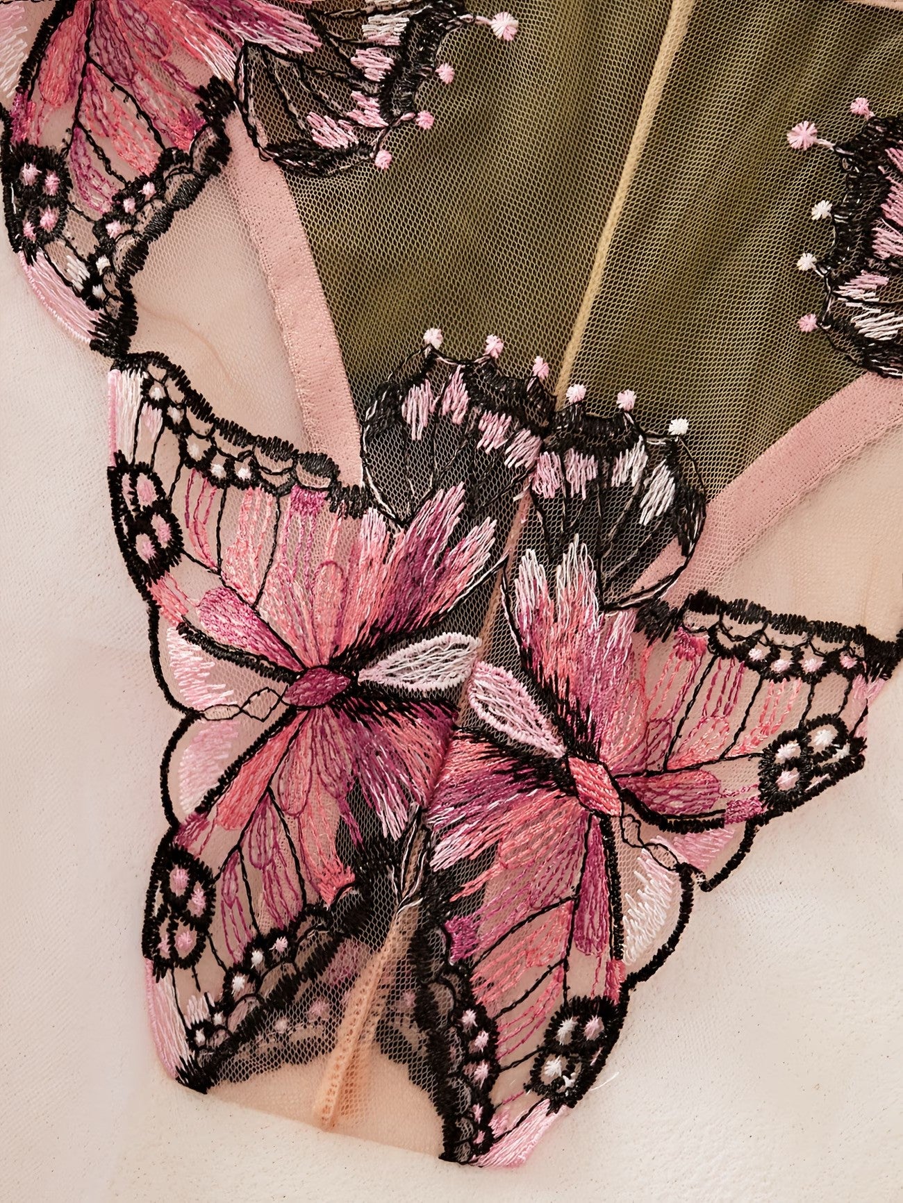 Close-up of a sheer pink mesh lingerie bottom with large embroidered butterfly motifs in pink, black, and white, plus a pale peach lining.